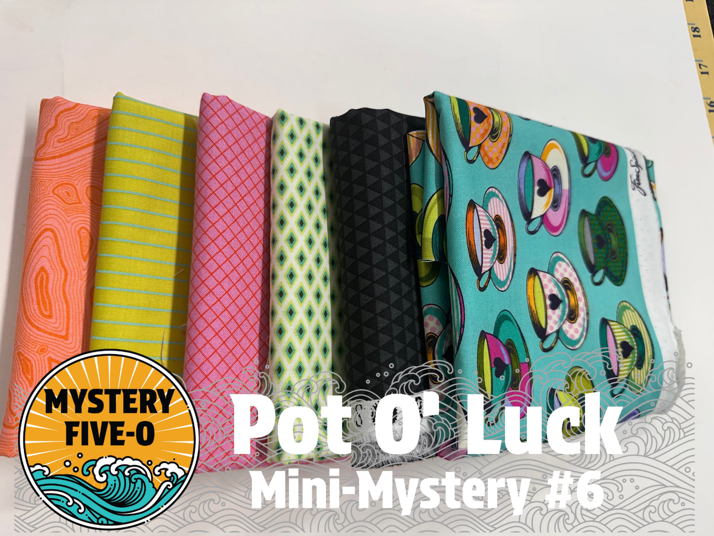 Six folded fabric samples in different patterns and colors are lined up on a white surface. The fabrics include orange, lime green, pink, light green, black, and turquoise with teacup prints.