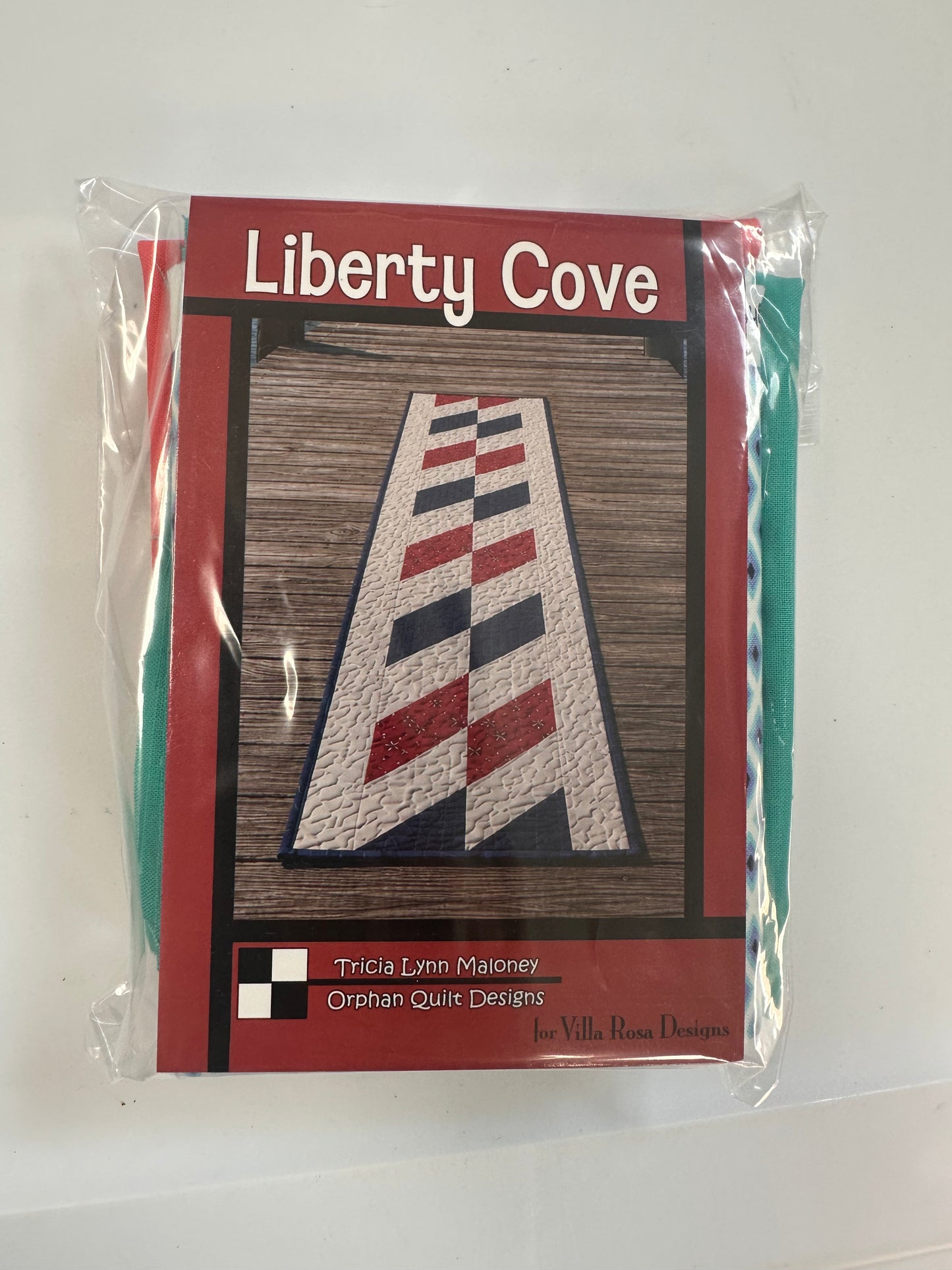 A packaged tape-runner pattern for 'Liberty Cove' by Tricia Lynn Maloney of Orphan Quilt Designs, and fabrics for runner and binding.