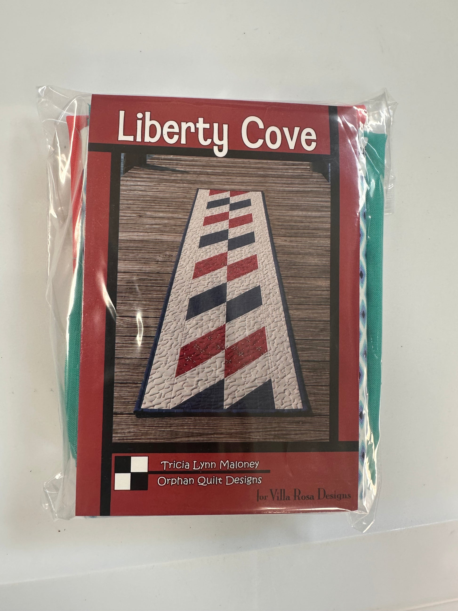 A packaged tape-runner pattern for 'Liberty Cove' by Tricia Lynn Maloney of Orphan Quilt Designs, and fabrics for runner and binding.