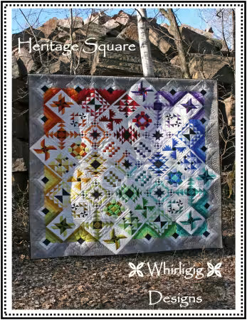 A square quilt with a complex geometric patchwork design in many colors,  featuring a rainbow gradient transitioning from warm tones on the left to cool tones on the right, with a gray border.