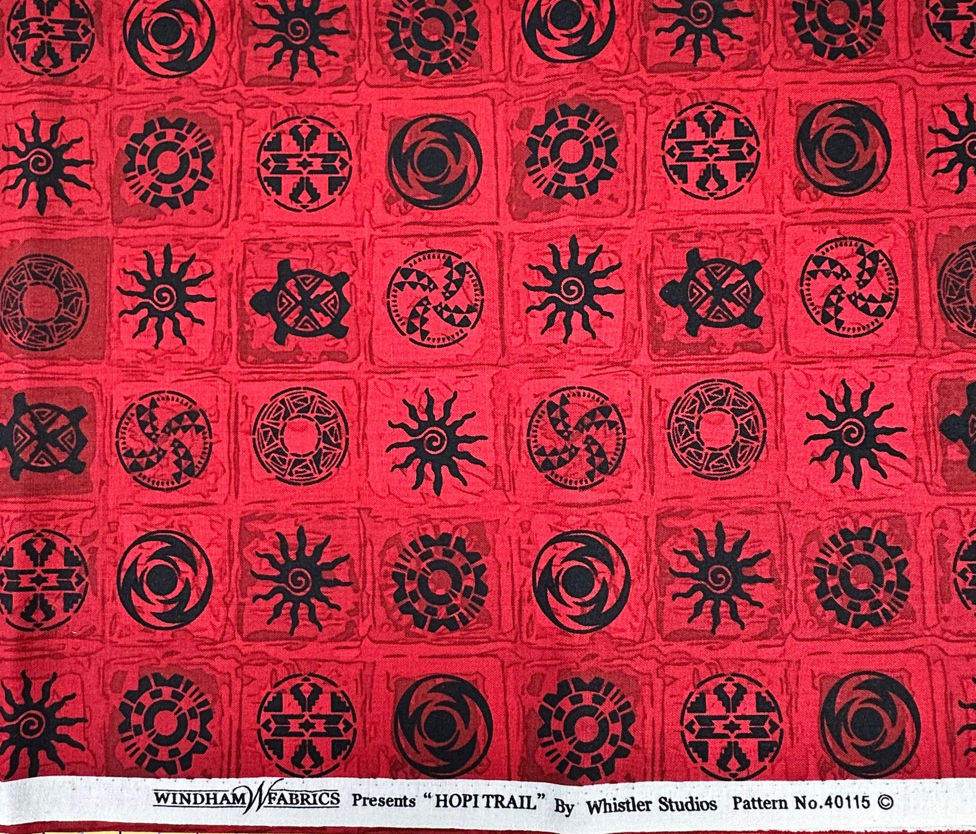 Red fabric with black geometric patterns in a grid layout.