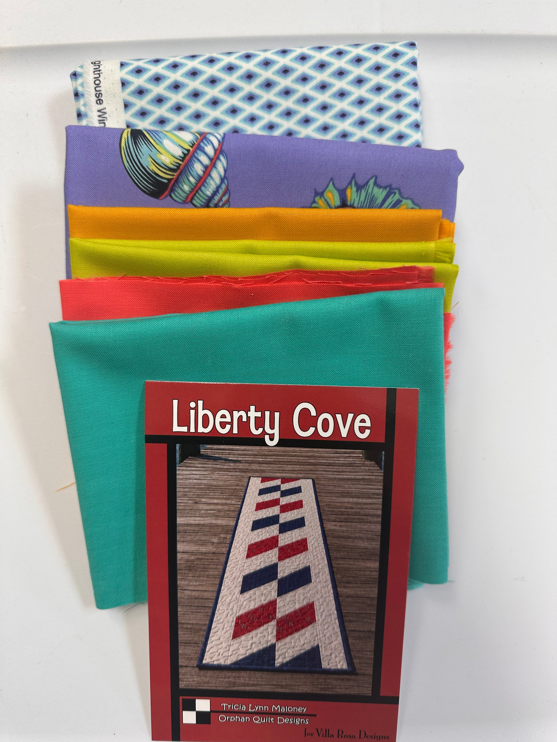 A stack of colorful fabric squares with printed patterns, partially fanned out behind a printed card titled "Liberty Cove" on a white background.