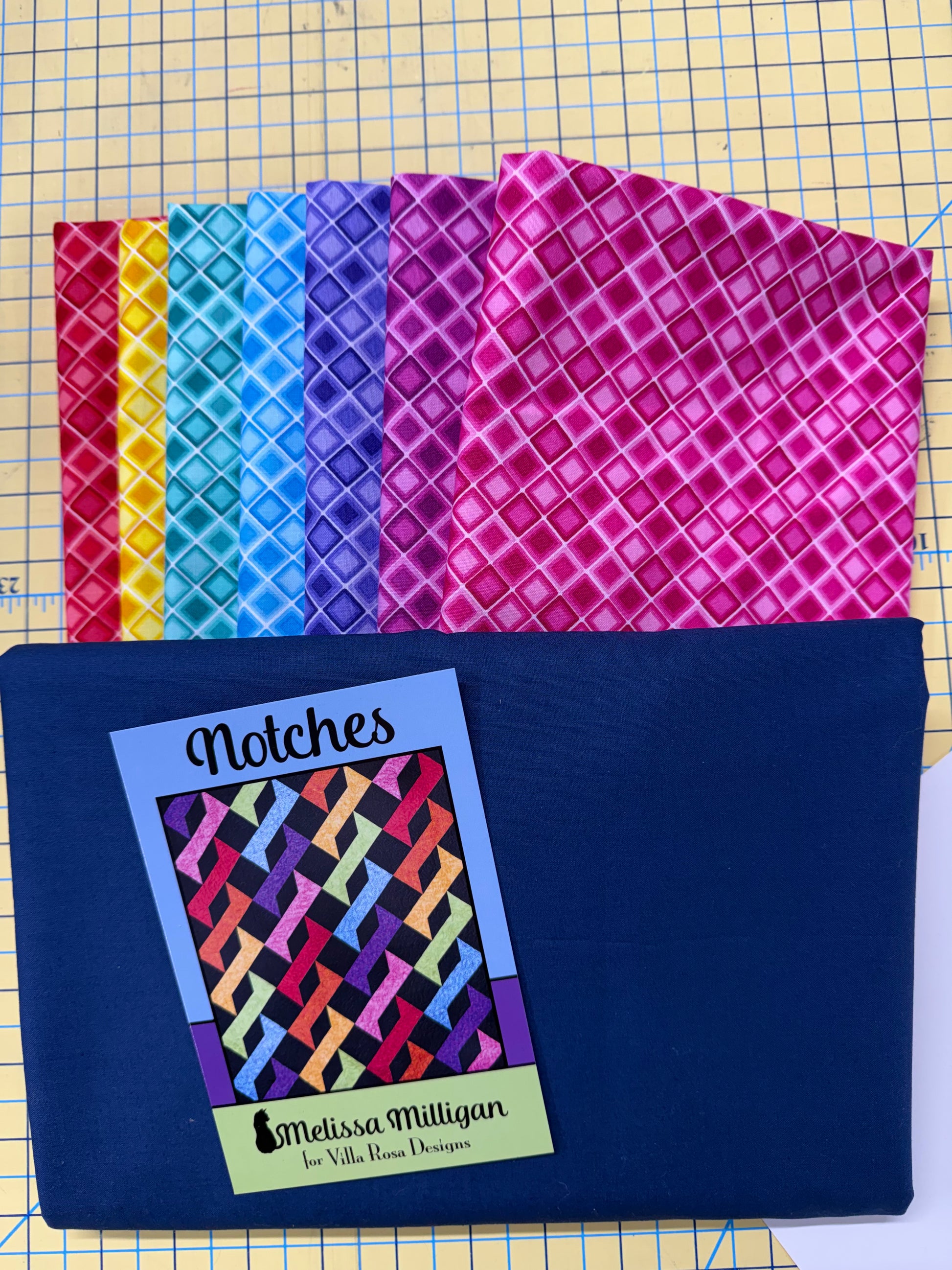 Stack of rainbow  fabrics with a blue for background and binding labeled and Notches Pattern