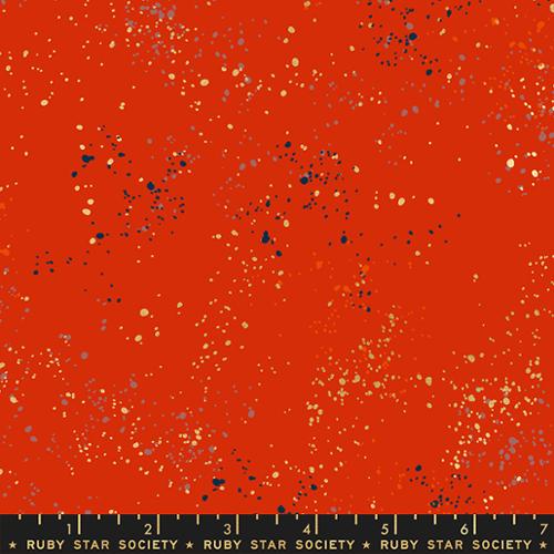 A close-up of a fabric or material swatch with a bright orange-red base covered in scattered speckles in black, beige, and muted blue-gray. 