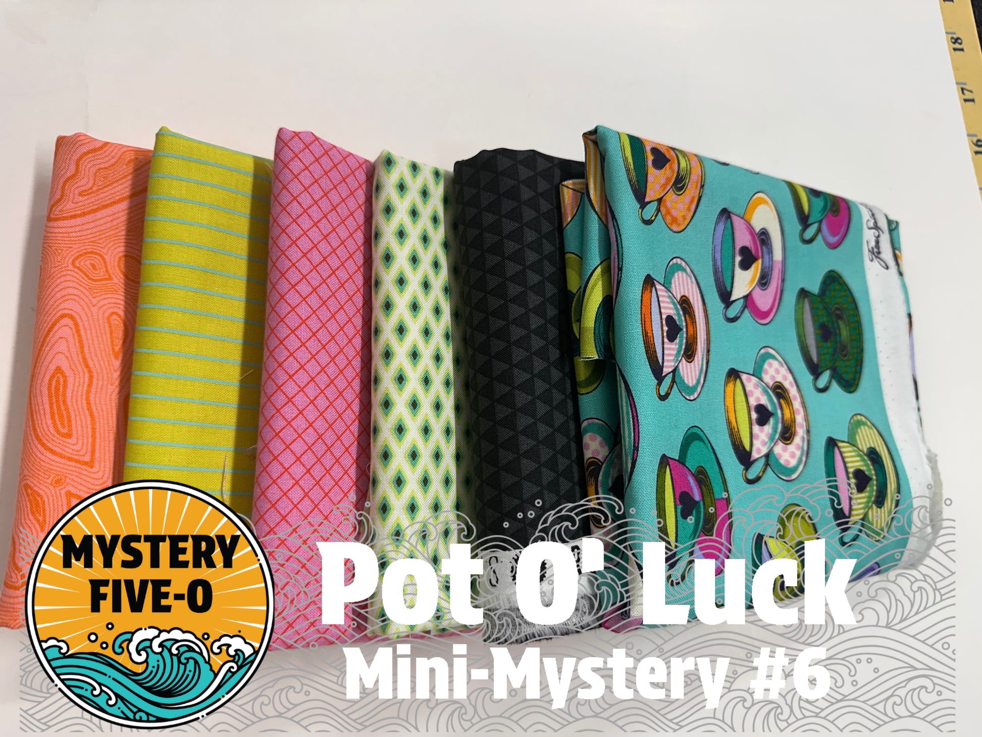Six folded fabric samples in different patterns and colors are lined up on a white surface. The fabrics include orange, lime green, pink, light green, black, and turquoise with teacup prints.